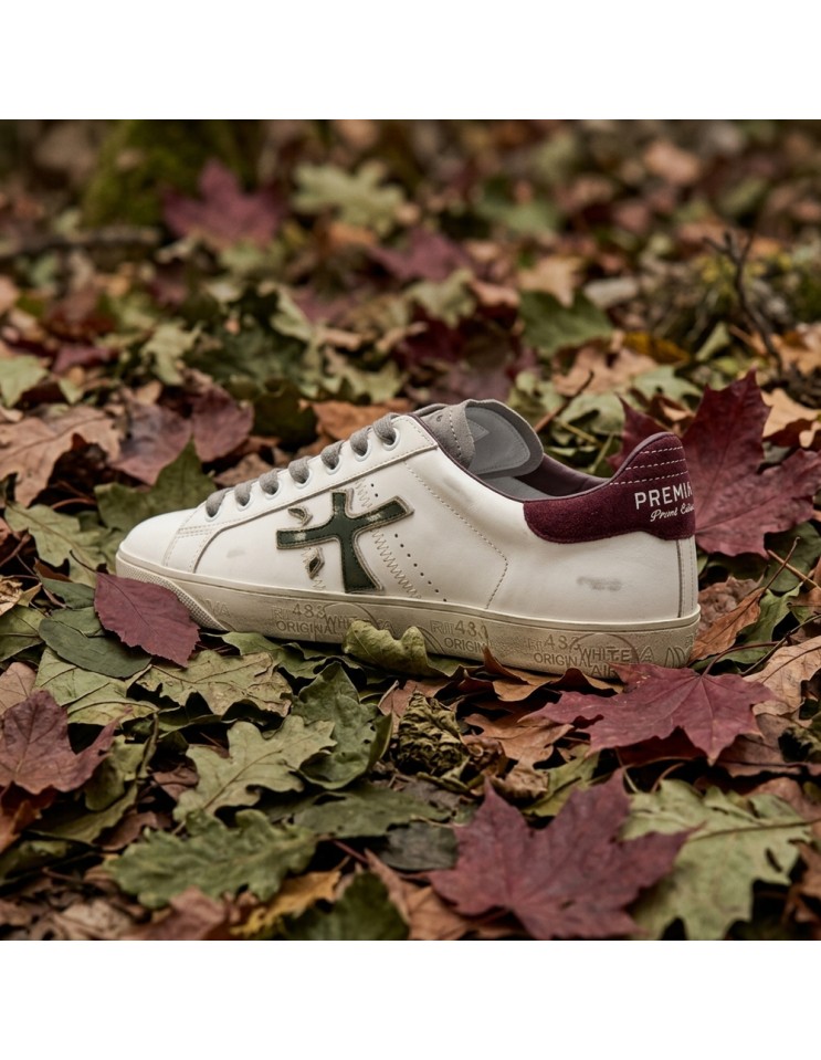 Premiata Steven print edition logo verde desgastado y talonera en ante granate dos pies sobre hojas vista desde atras
