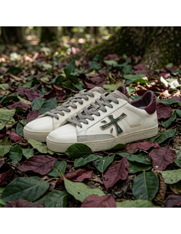 Premiata Steven print edition logo verde desgastado y talonera en ante granate dos pies sobre hojas de colores dos pies