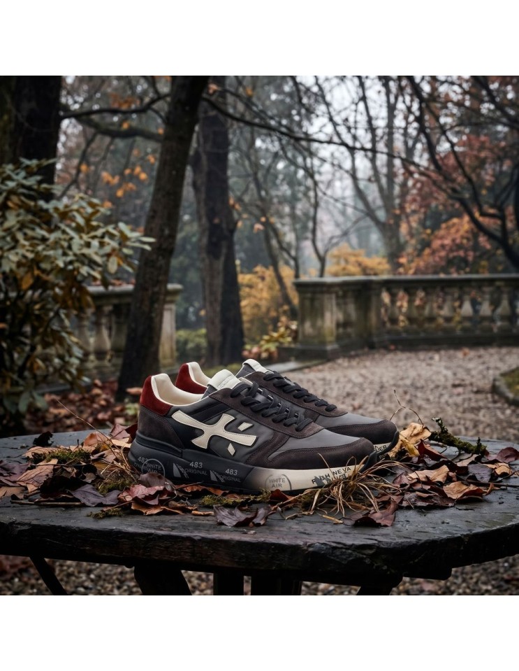 Premiata Mick negro gris y talonera roja vista otoñal, sobre base de piedra y hojas